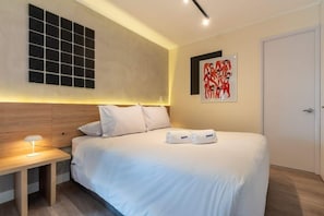Une chambre d’hôtel avec un lit, une table de chevet, une œuvre d’art accrochée au mur et une porte.