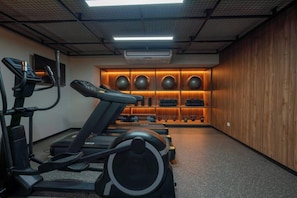 Une salle de sport équipée de tapis de course, de vélos elliptiques et d’un mur entier dédié au matériel d’exercice.