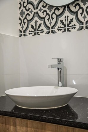 Ein Badezimmer mit einem weißen Keramikwaschbecken, einem modernen Wasserhahn und einer schwarzen und weißen Fliesenspiegelverkleidung.