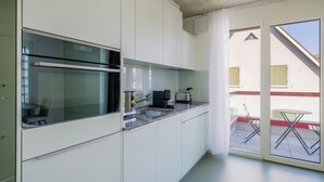 Moderni keittiö, jossa on sisäänrakennettu uuni, kahvinkeitin ja leivänpaahdin. Ikkunasta avautuu näkymä ulkona olevaan rakennukseen.