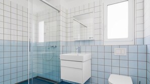 Kylpyhuone, jossa on lasiseinäinen suihkukaappi, valkoinen pesuallas ja wc-istuin.