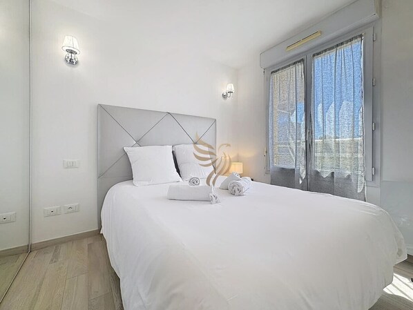 A modern bedroom with a large bed, white bedding, a geometric headboard, and two wall-mounted lights.