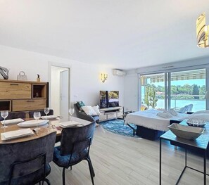 A modern hotel room with a dining area, a sofa, a TV, and a large window with a view of the sea. - Serenity Getaway–4 people–WiFi–Terrace–Garage (Saint-Raphaël)