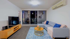 A modern living room with a flat-screen TV, a grey sofa, a wooden entertainment unit, and a blue patterned rug.