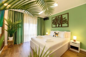 Ein Hotelzimmer mit einem großen Bett, grünen Vorhängen, einem Blumentopf und einer Wand mit gerahmten Kunstwerken.