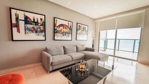Una sala moderna con un sofá seccional gris, una mesa de centro de vidrio con botellas y tres cuadros abstractos en la pared.