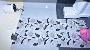 Een badkamer met een achterwand van bloementegels, een wit toilet, een roze waterfles en een witte kraan.