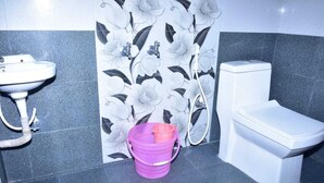 Een badkamer met een wit wastafel, een toilet en een paarse emmer op de vloer.