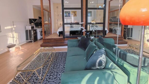 A modern living room with a green sofa, a patterned rug, and a glass door leading to a kitchen and dining area. - Shanghai Hills & Zinn Sunshine bnb (Shanghai)