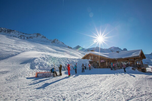 A wooden lodge with a snow-covered roof, a sign reading "PAUSE," and a ski slope in the background.