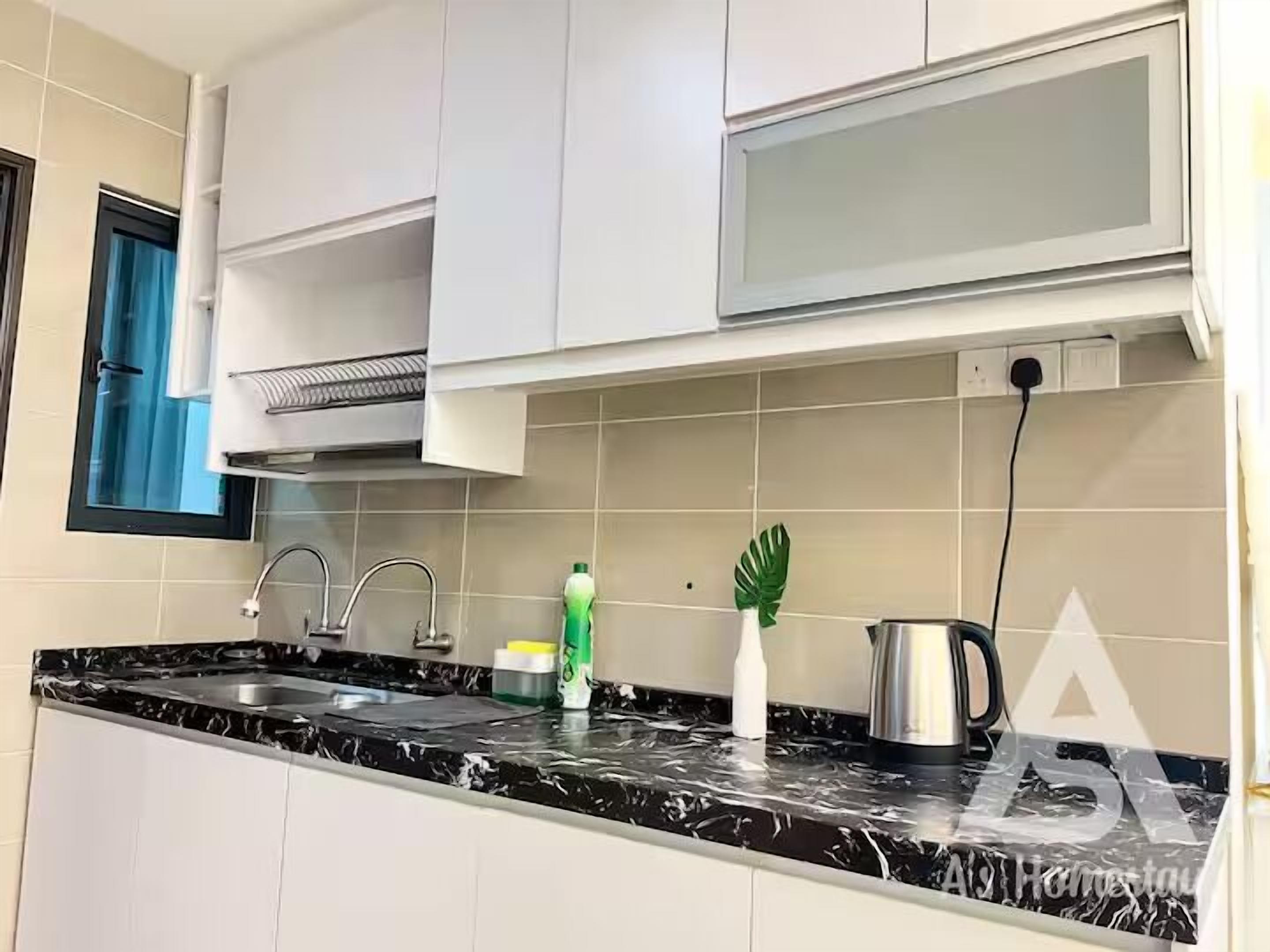 A modern kitchen with white cabinets, a black marble countertop, a sink, and a window with blue curtains.