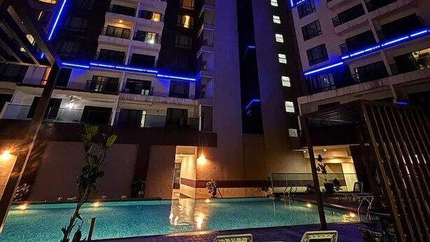 Un immeuble de grande hauteur, agrémenté de lignes bleues illuminées, et un espace piscine avec des chaises longues.