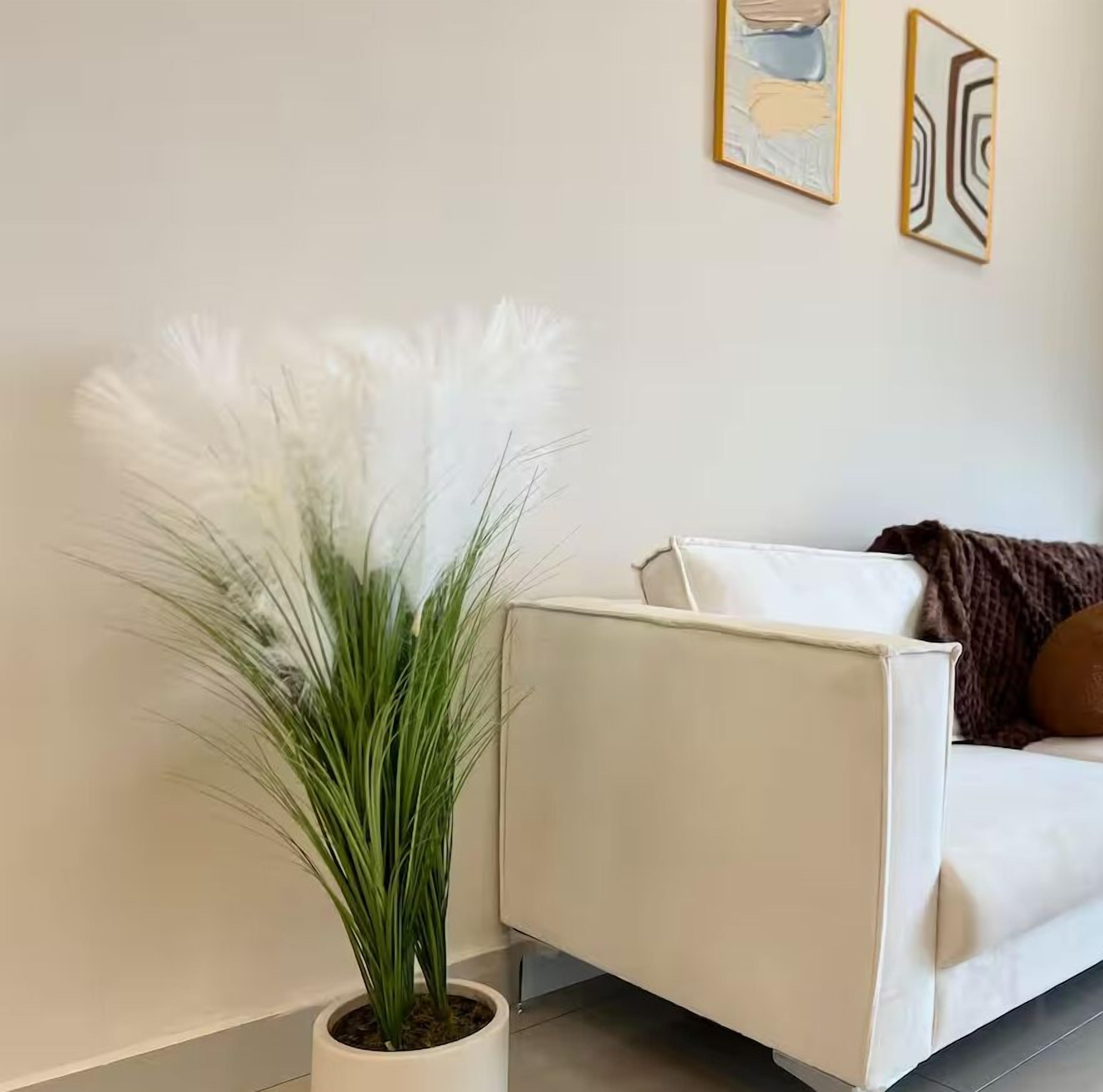 Un canapé blanc avec un coussin marron, une plante en pot blanche aux feuilles vertes et une œuvre d’art abstraite accrochée au mur.