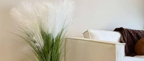 Un canapé blanc avec un coussin marron, une plante en pot blanche aux feuilles vertes et une œuvre d’art abstraite accrochée au mur.
