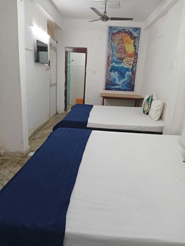 A room with two single beds, a ceiling fan, a painting on the wall, and a small table.
