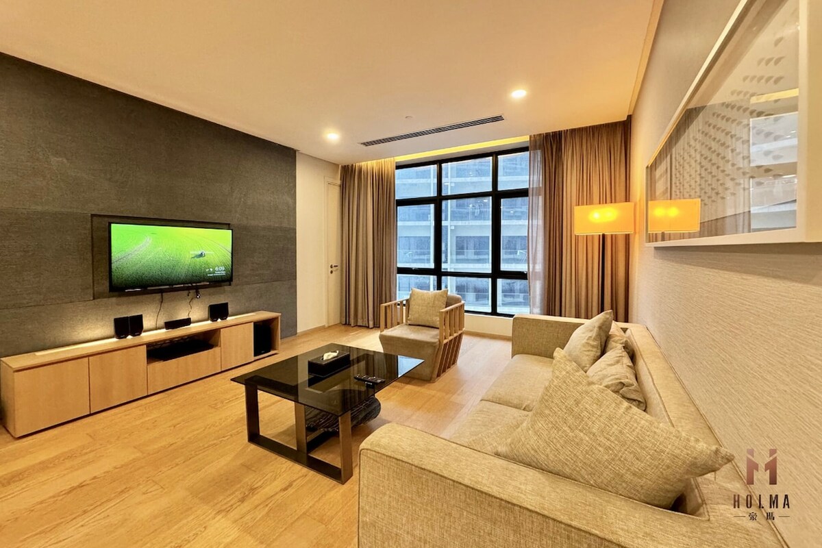 A modern living room with a flat-screen TV, wooden entertainment unit, sofa, and a large window with curtains.