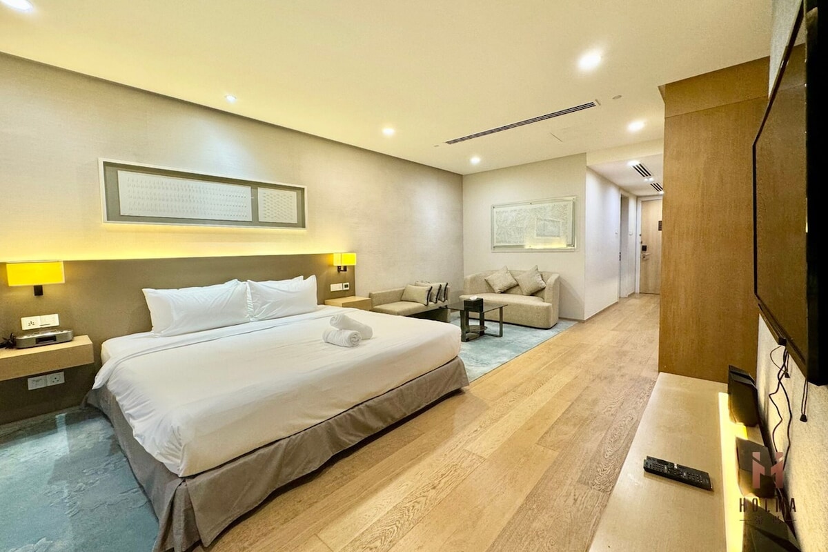 A modern hotel room with a large bed, a sofa, a TV, and a desk.