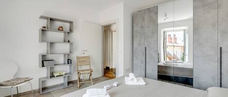Quarto de hotel moderno com uma cama grande, guarda-roupa embutido, área de estar com uma poltrona e vista para o exterior.