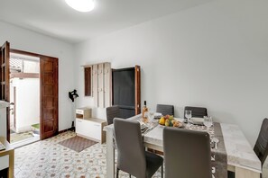 A dining area with a table set for four, a fruit bowl, and a bottle of wine.