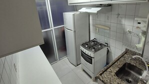 Une cuisine de taille réduite, avec des meubles blancs, une cuisinière à gaz, un réfrigérateur et un évier.