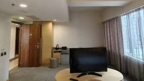 A hotel room with a television, a small kitchenette, a wooden door, and a window with curtains. - H1 hotel (Kowloon)