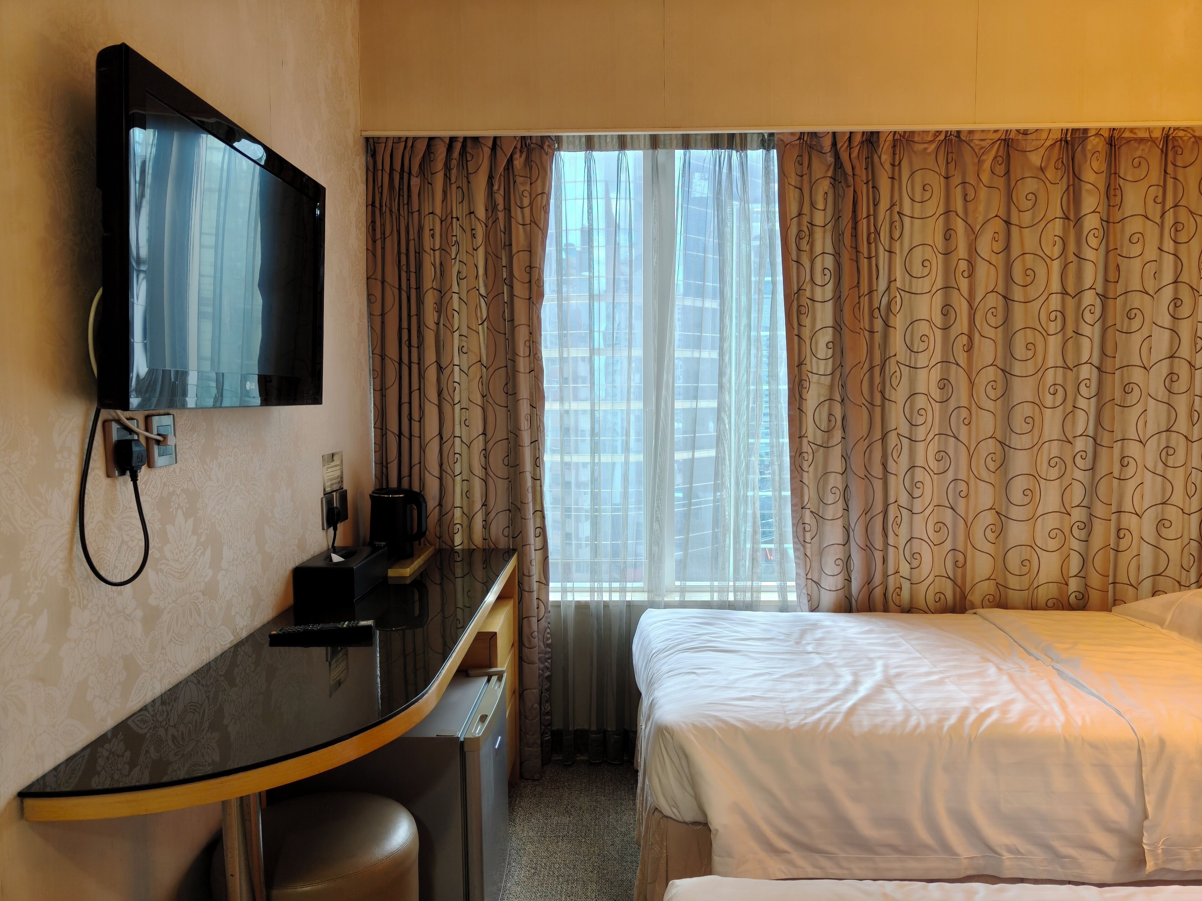 Ein Hotelzimmer mit Bett, Schreibtisch mit Fernseher, Kaffeemaschine und einem Fenster mit Vorhängen.