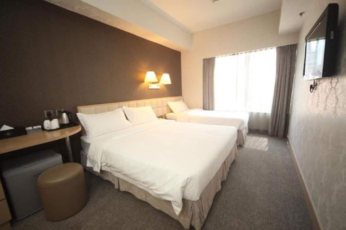 A hotel room with two beds, a desk, a chair, a small table, a TV, and a window with curtains.