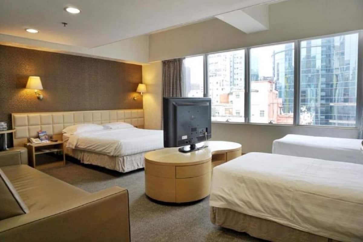A hotel room with two beds, a TV, a round wooden table, and a sofa.
