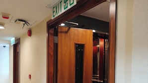 A hotel corridor with an exit door, a fire alarm, and a ceiling light. - H1 hotel (Kowloon)