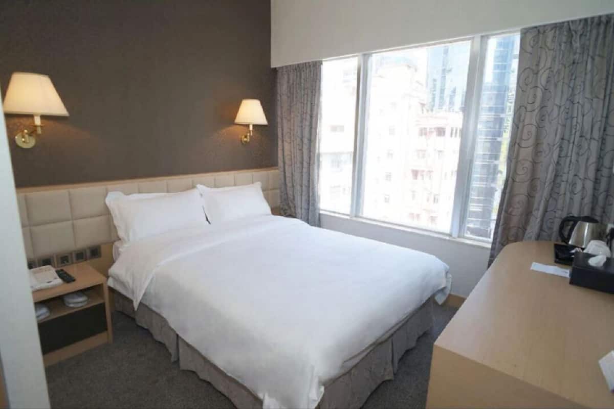 A hotel room with a bed, bedside tables, lamps, a desk, and a window with curtains.