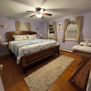 Une chambre à coucher avec un lit en bois, un ventilateur de plafond, une fenêtre avec des rideaux et un radiateur.