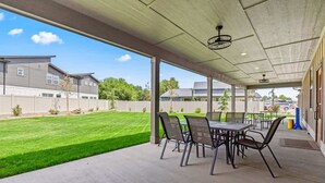 A covered patio area with a table and chairs, a concrete floor, and a view of a well-maintained lawn and neighboring houses.