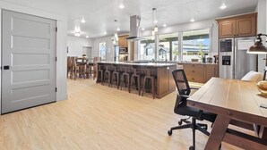 A modern kitchen with a central island, bar stools, and a dining table with chairs.