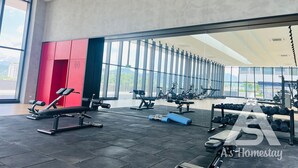 A modern gym with various exercise equipment, large windows, and a view of the city.