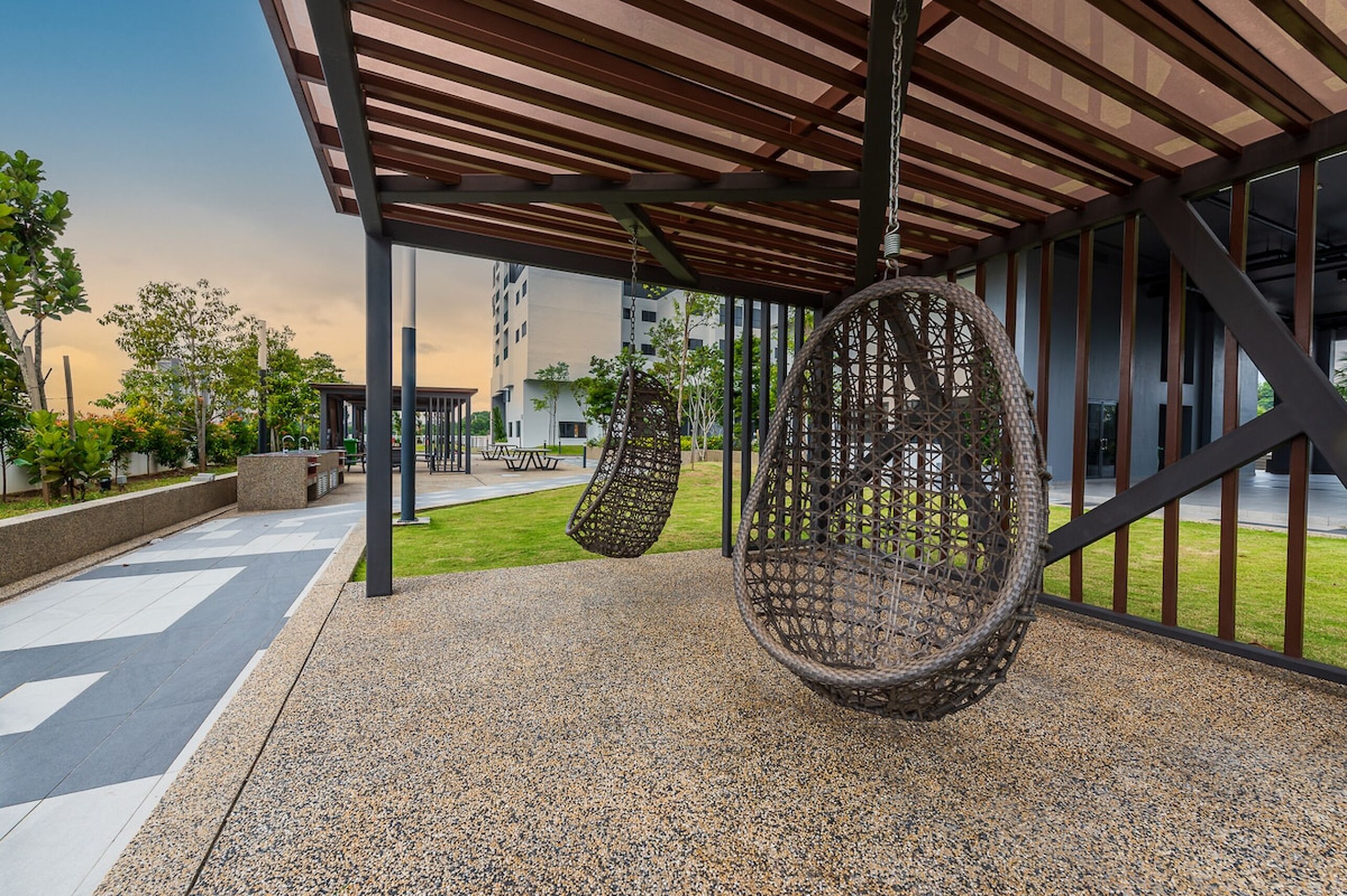 Un área de estar al aire libre con sillones colgantes, un porche cubierto y vistas de edificios residenciales al fondo.