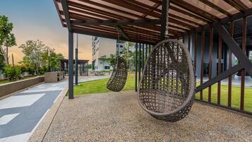 Un área de estar al aire libre con sillones colgantes, un porche cubierto y vistas de edificios residenciales al fondo.