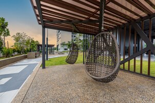 Un área de estar al aire libre con sillones colgantes, un porche cubierto y vistas de edificios residenciales al fondo.