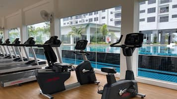 A gym with treadmills, stationary bikes, and an elliptical machine. It has large windows with a view of a swimming pool and a building with balconies.