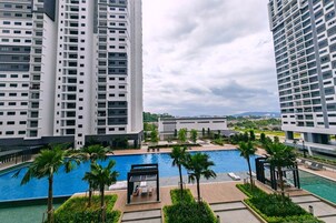 A modern high-rise building with a rooftop pool area, surrounded by lush greenery and palm trees.