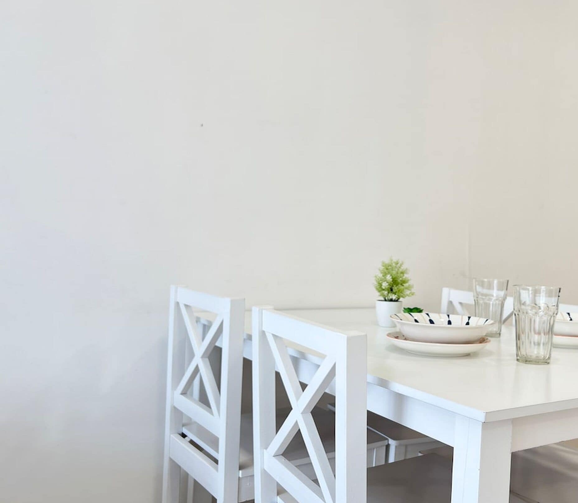 A white dining table with four chairs, a small potted plant, and several clear glasses on the table.