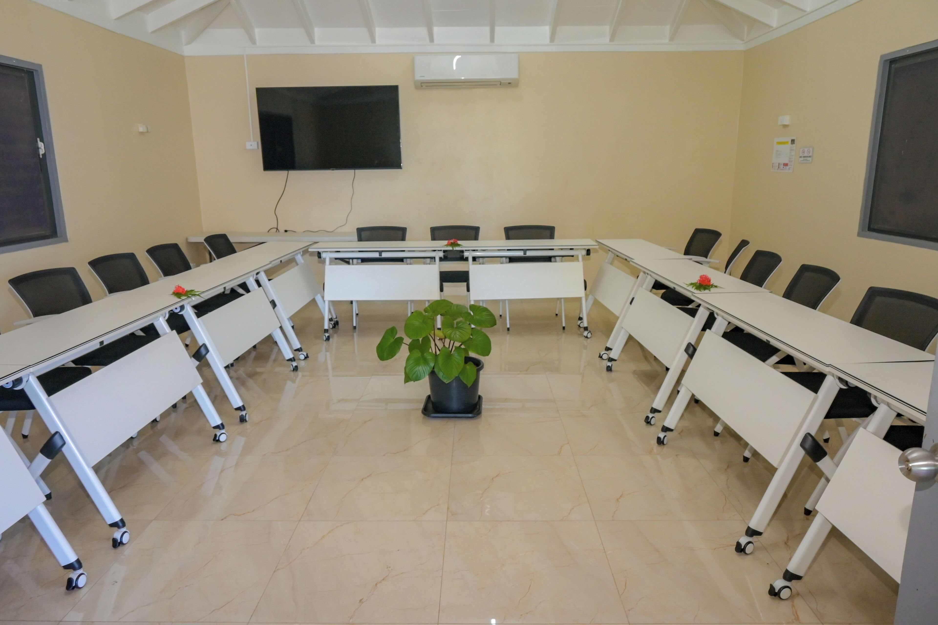 A conference room with a long table, chairs, a potted plant, and a mounted TV.