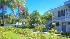 Un hotel de dos pisos, un jardín cuidado con diversas plantas y flores, y un cielo azul despejado.
