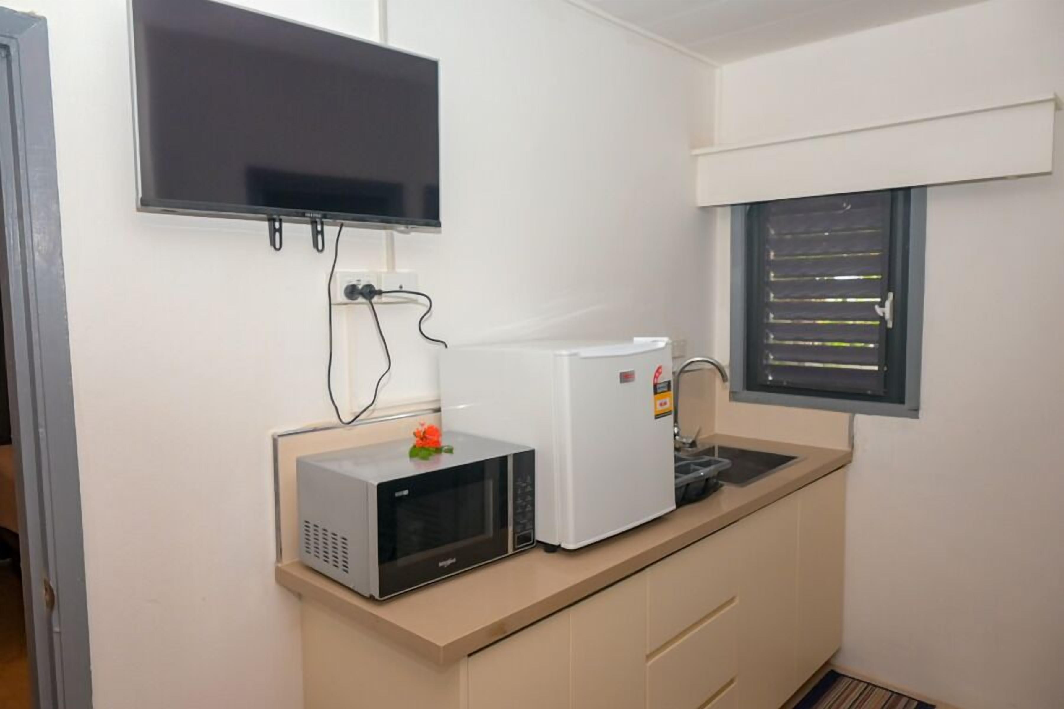 A kitchenette with a microwave, a small refrigerator, a sink, and a flat-screen TV mounted on the wall.