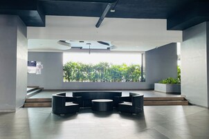 A modern lobby with a seating area, a staircase, and a large window with a view of greenery.