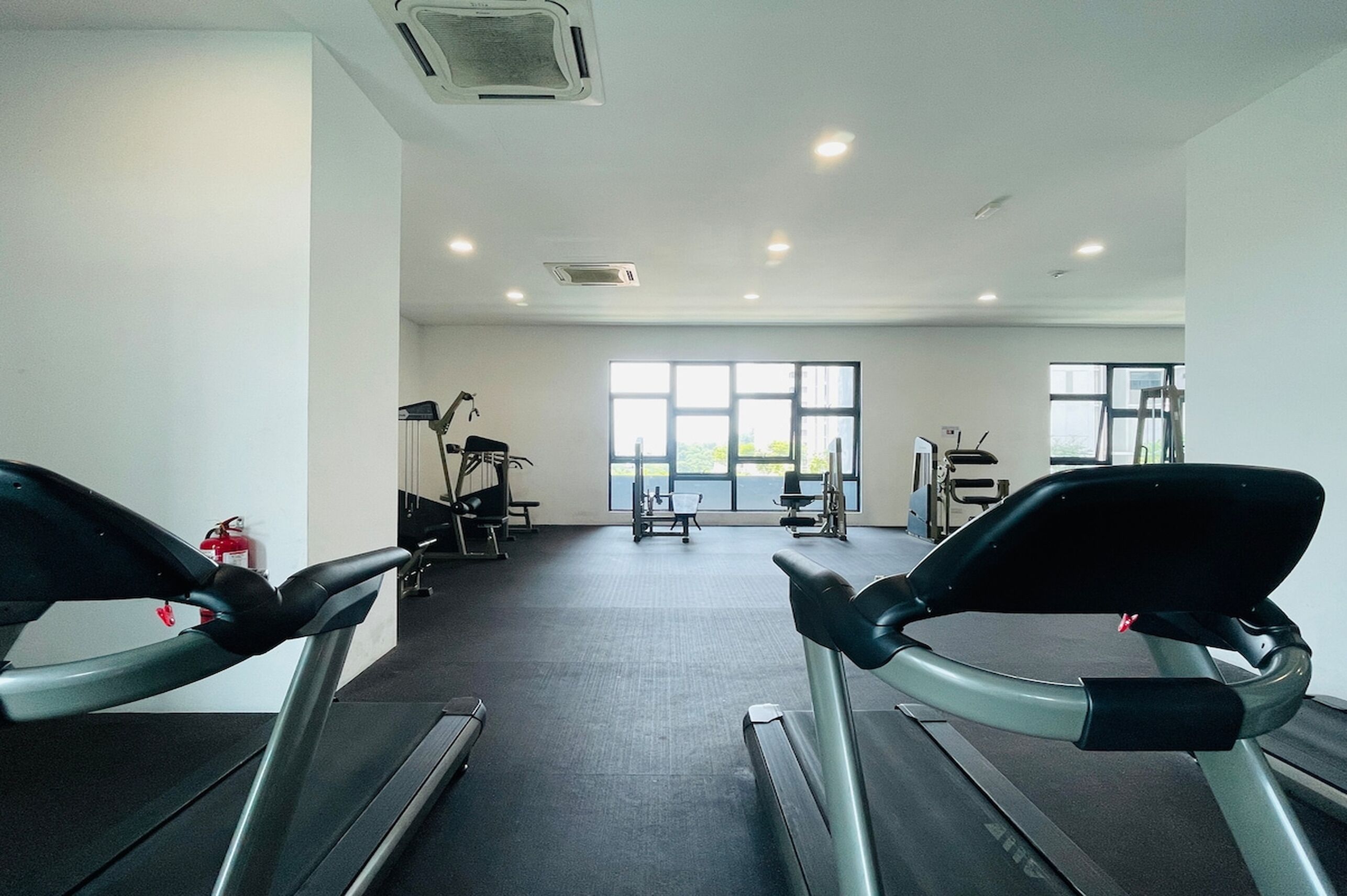 Een sportschool met loopbanden, trainingsapparatuur en grote ramen voor natuurlijk licht.
