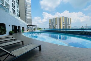 A modern hotel with a rooftop pool, lounge chairs, and a view of high-rise buildings.