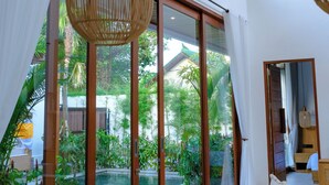 Una habitación moderna con un amplio ventanal corredero que da a una zona de piscina, una mesa de comedor de madera y una lámpara colgante de mimbre.
