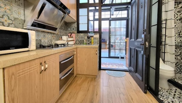 A kitchen with wooden cabinets, a microwave, and a large window. - Shanghai Hills & Zinn Happy Family Bnb (Shanghai)