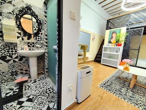 A bathroom with a black and white patterned tile floor, a white sink, and a mirror with a decorative frame. There is a white heater on the floor and a small table with a vase of flowers.