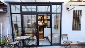 A glass-enclosed patio with a table and chairs, a small seating area, and a view into the interior of a building. - Shanghai Hills & Zinn Happy Family Bnb (Shanghai)